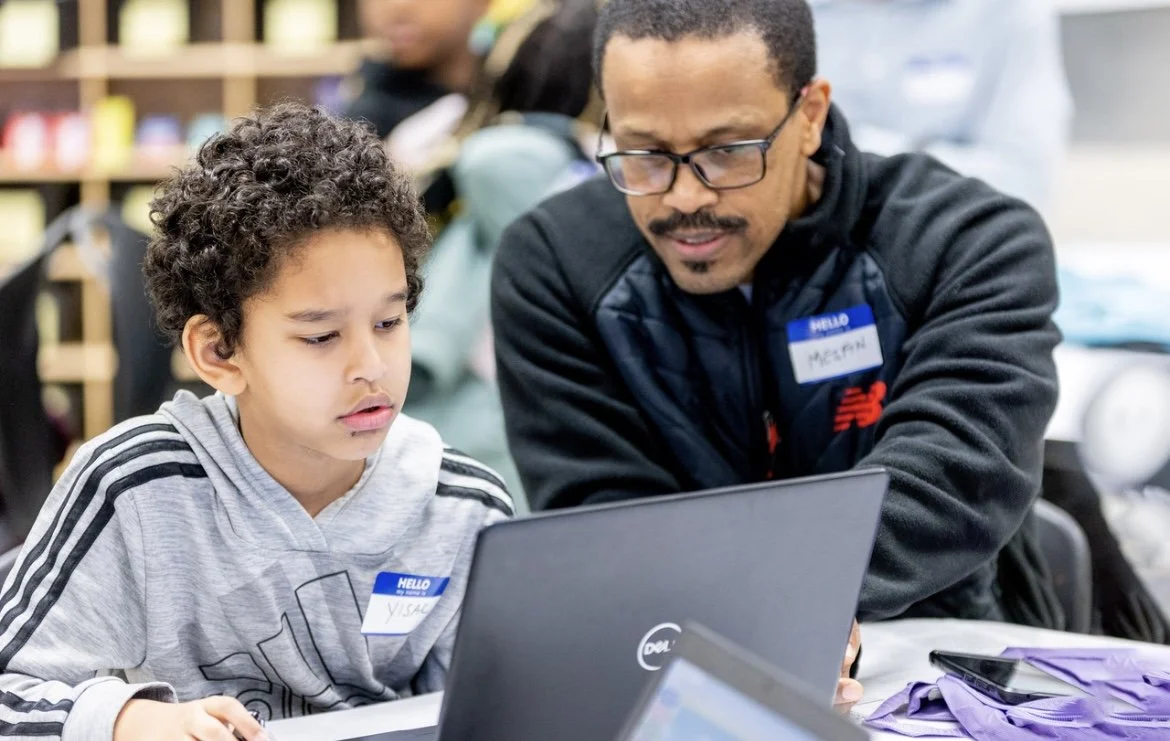 Adult volunteer helps a student use a laptop during an Inspiredu digital learning program.