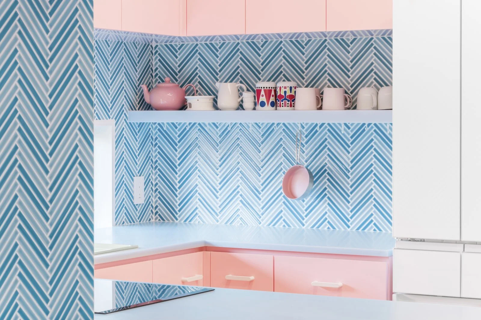 the-light-blue-tiles-of-the-kitchen-vary-in-color-and-are-arranged-in-a-graphically-arresting-herringbone-pattern-that-offers-a-pleasant-respite-from-the-cotton-candy-pink-of-the-cabinetry.jpg
