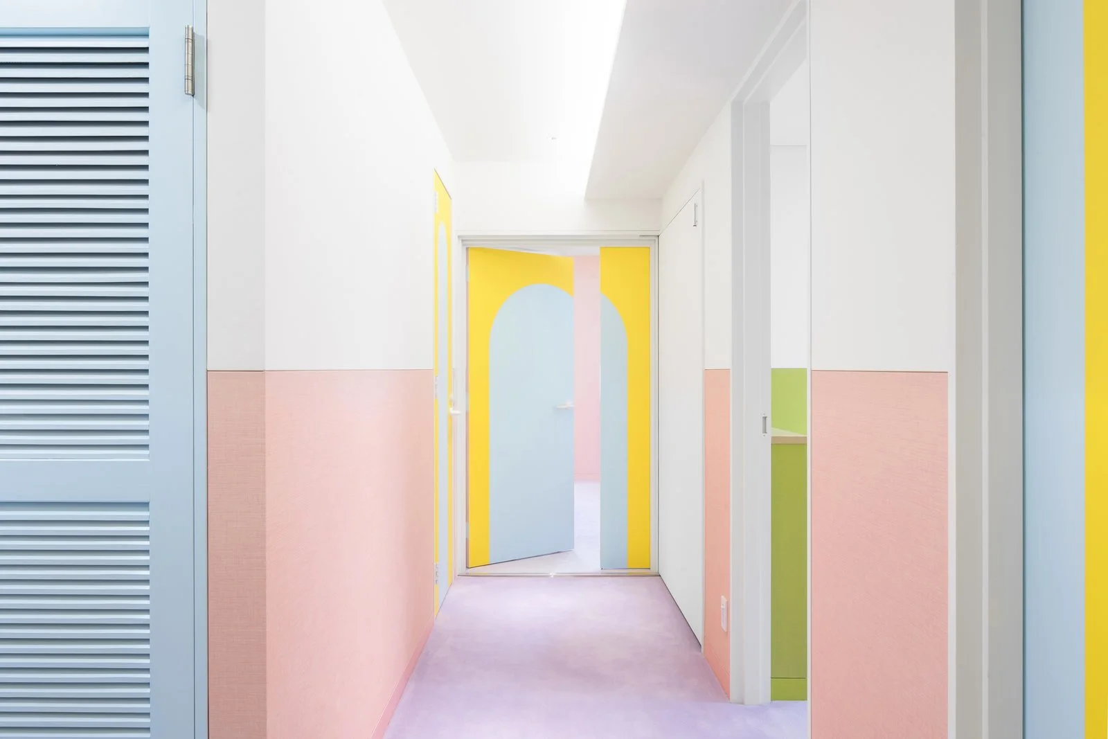 walls-in-the-corridor-are-lined-with-pink-wainscotting-while-the-white-upper-portion-provides-a-moment-of-visual-relief-and-balance-a-vibrant-yellow-at-the-end-of-the-corridor-draws-the-eye-down-the-hallway.jpg