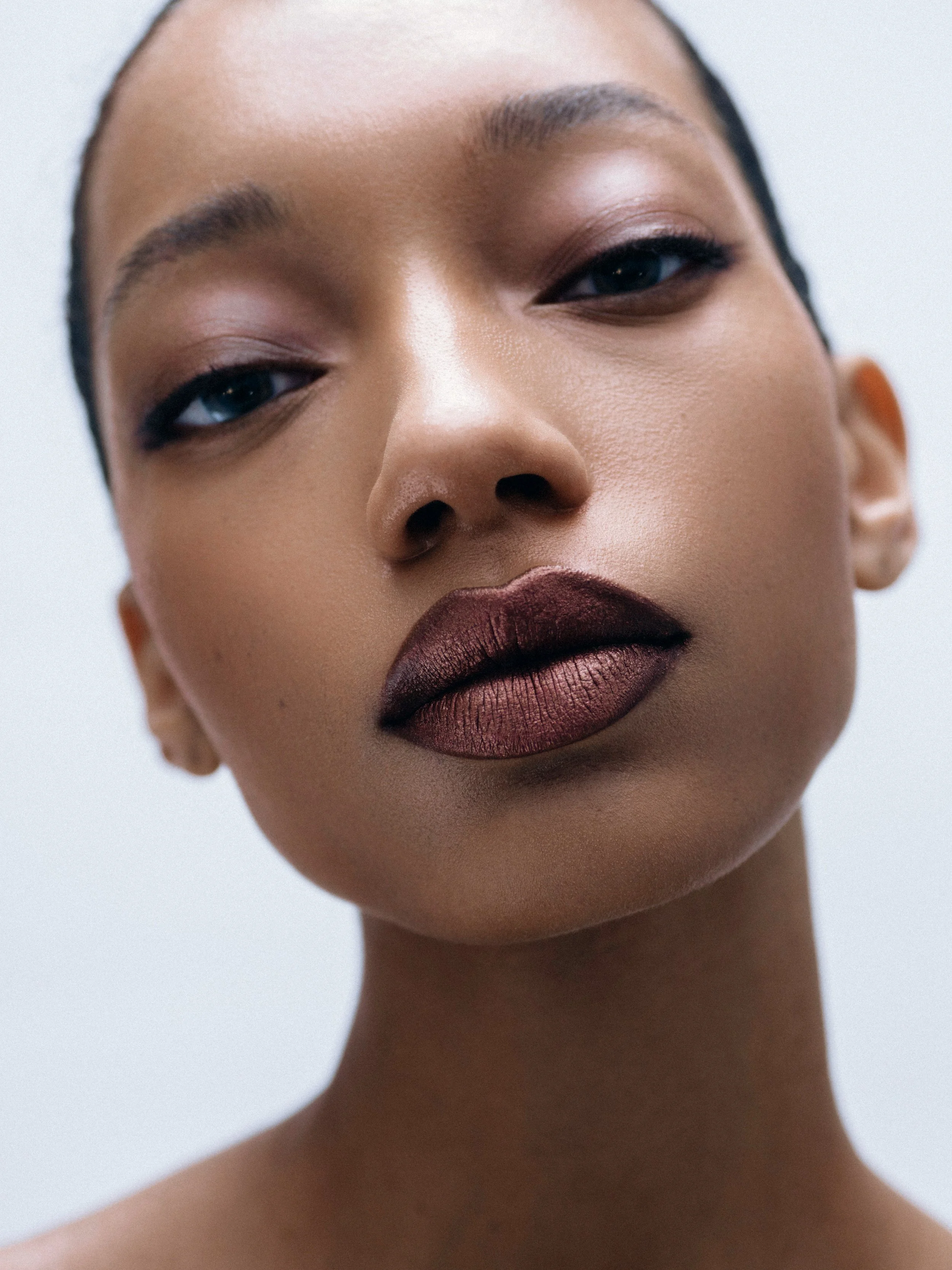 Close-up of a woman's face with smooth skin, natural makeup, bold dark lipstick, and arched eyebrows.