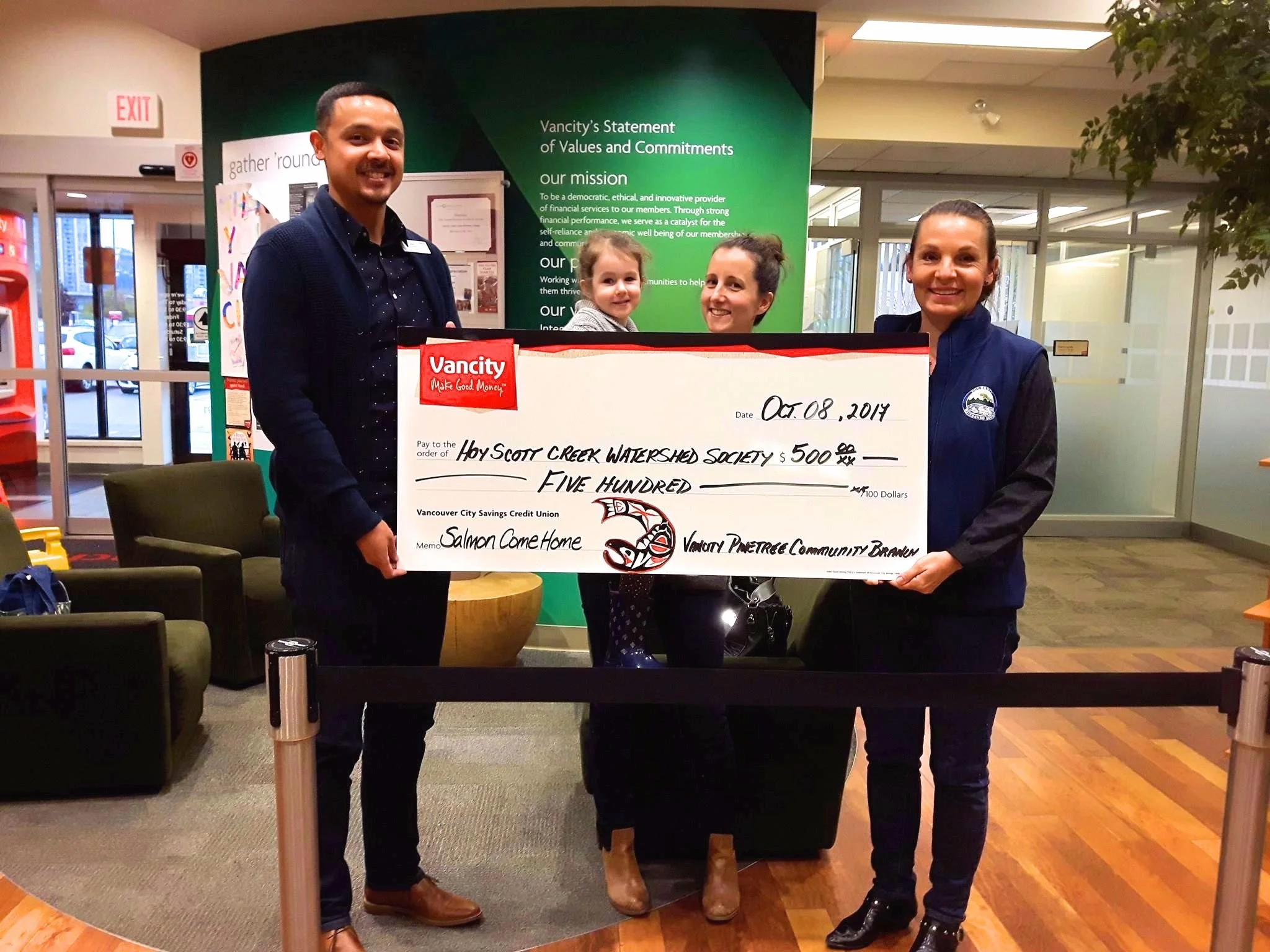 Vancity manager Omar (left) presents a $500 cheque to HSWS secretary Emily (center with daughter Joan) and HSWS president Robbin (right) for Salmon Come Home. 
