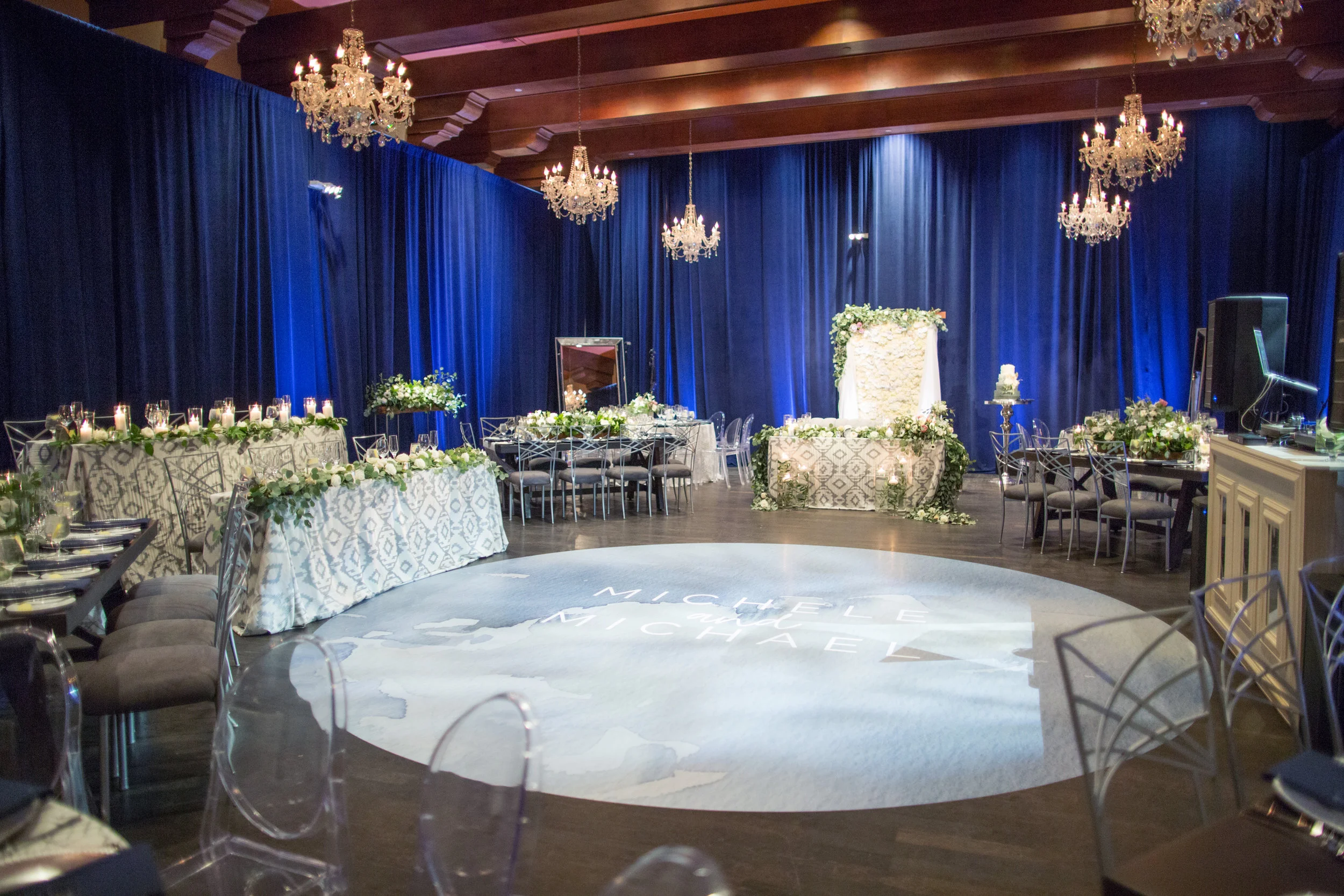 41 wedding reception blue velvet draped walls chandeliers wood beam ceiling custom dance floor decal bride groom name dance floor dinner reception white wedding flowers hydrangea backdrop Life Design Events photos by Melissa Jill Photography.jpg