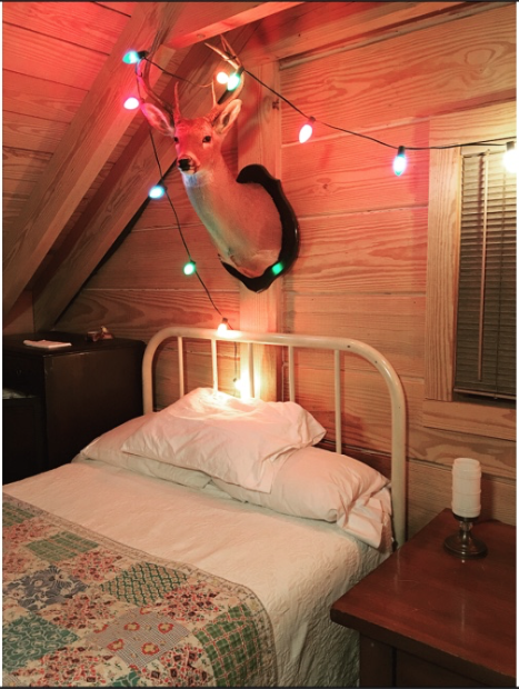 View of an iron bed in the loft featuring a handmade quilt, antique side lamp, and a trophy deer killed on our land.