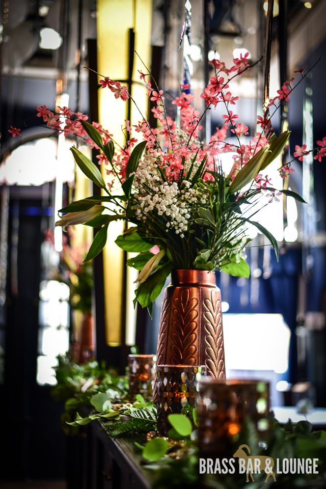 A rose gold metallic vase holding pink and white flowers with green leaves.