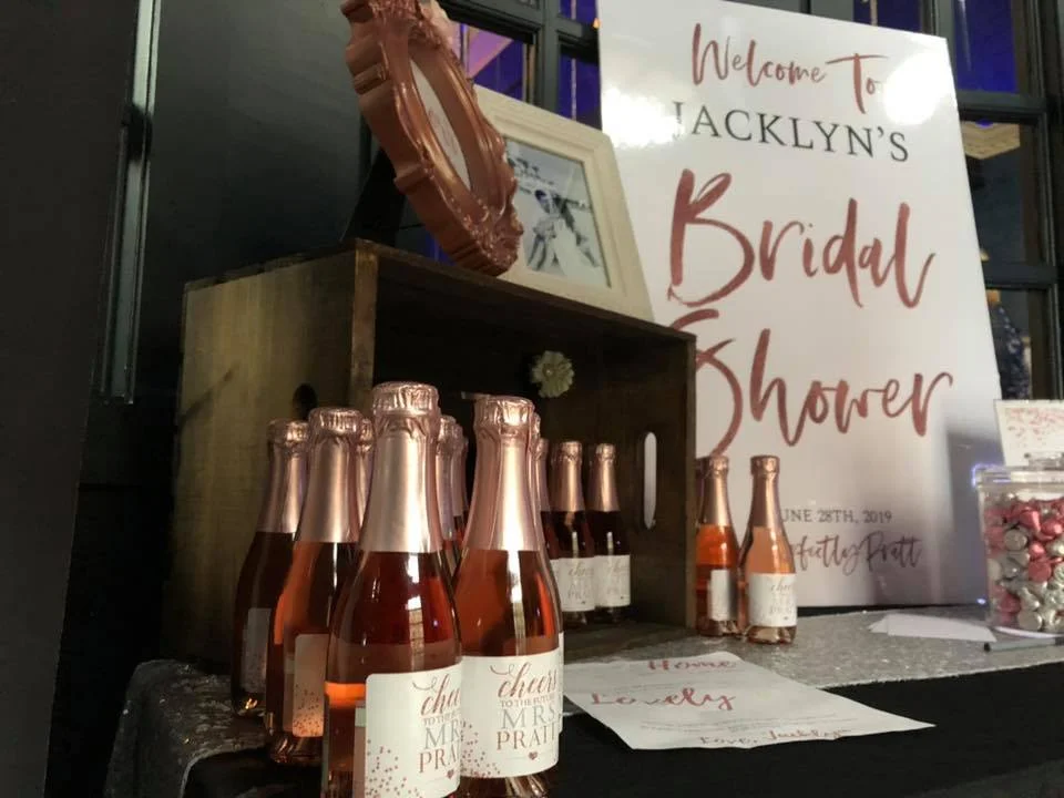 A table with bridal shower decorations including bottles of rose and party favors.