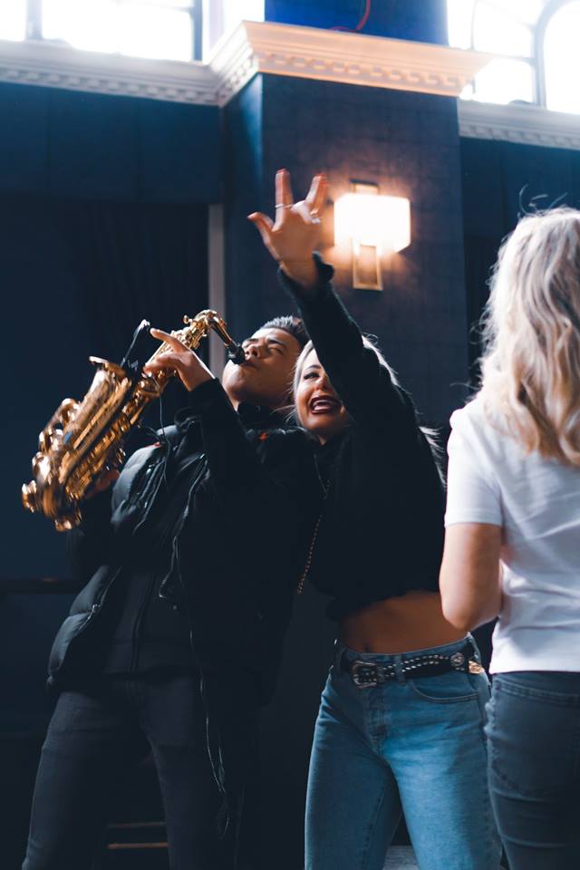 A girl grabbing the shoulder of a saxophone player.