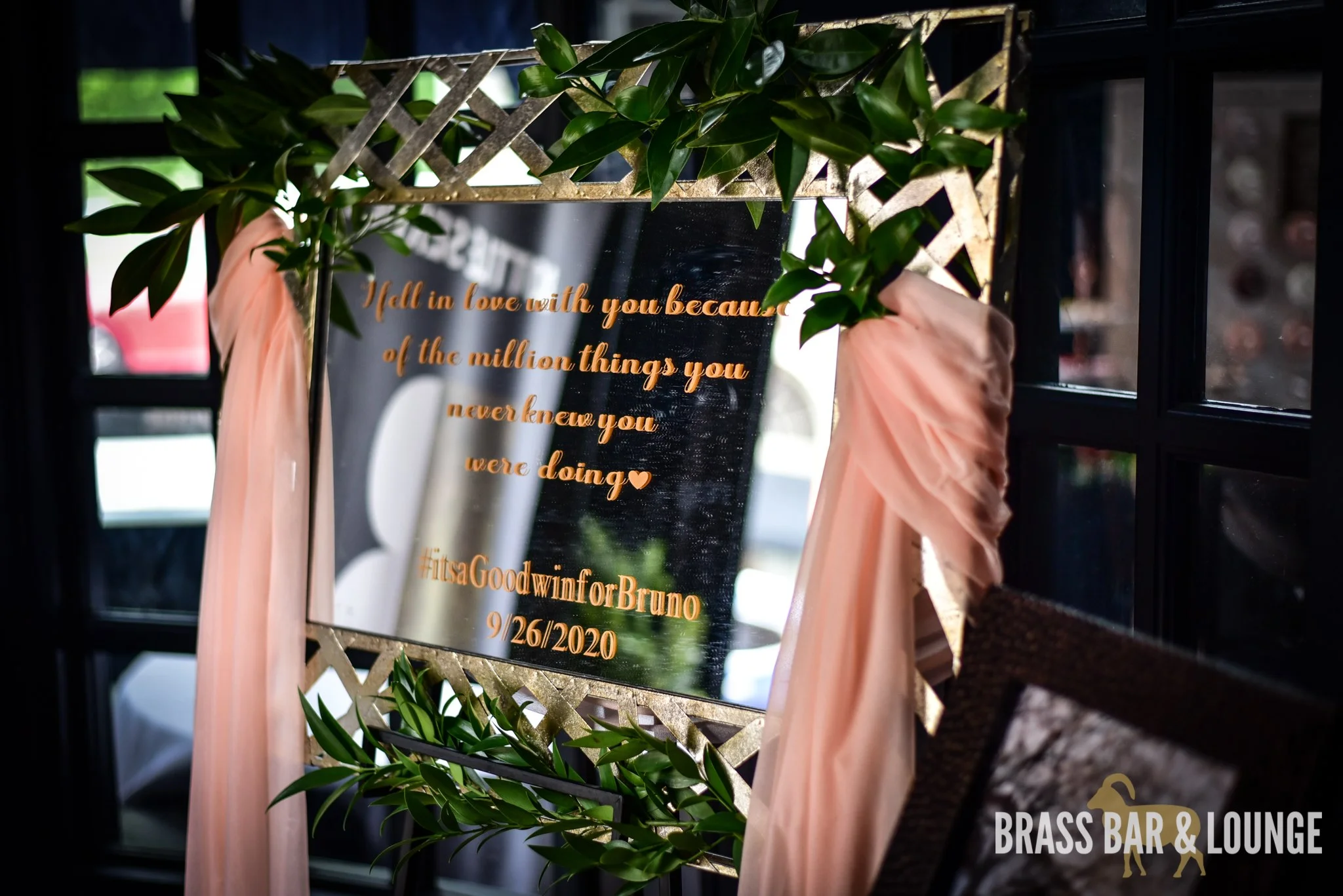 A gold mirror with a quote in the center decorated with pink and green.