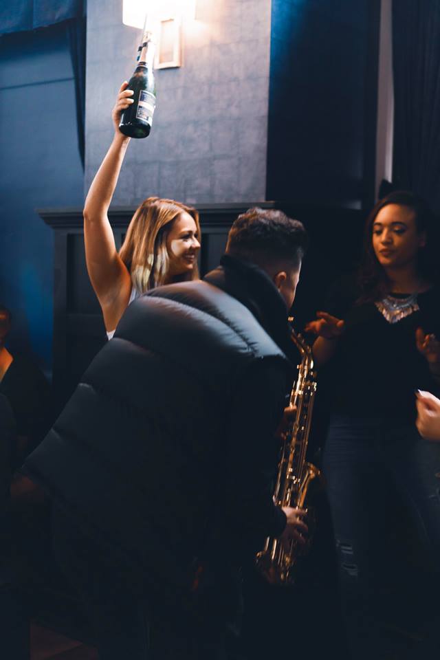 A man playing the saxophone with two girls in the background.