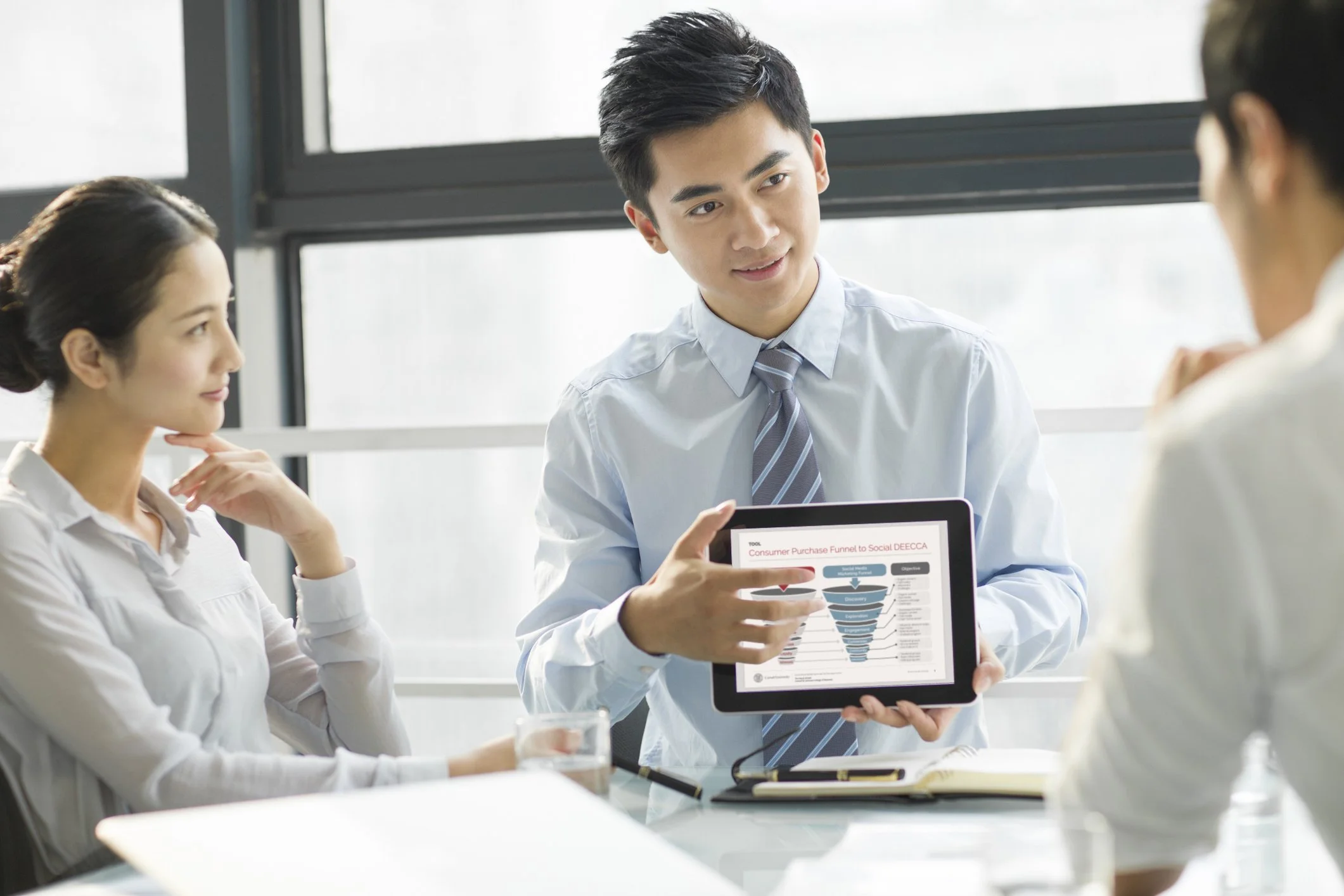 Business professionals discussing a consumer purchase funnel diagram displayed on a tablet during a team meeting.