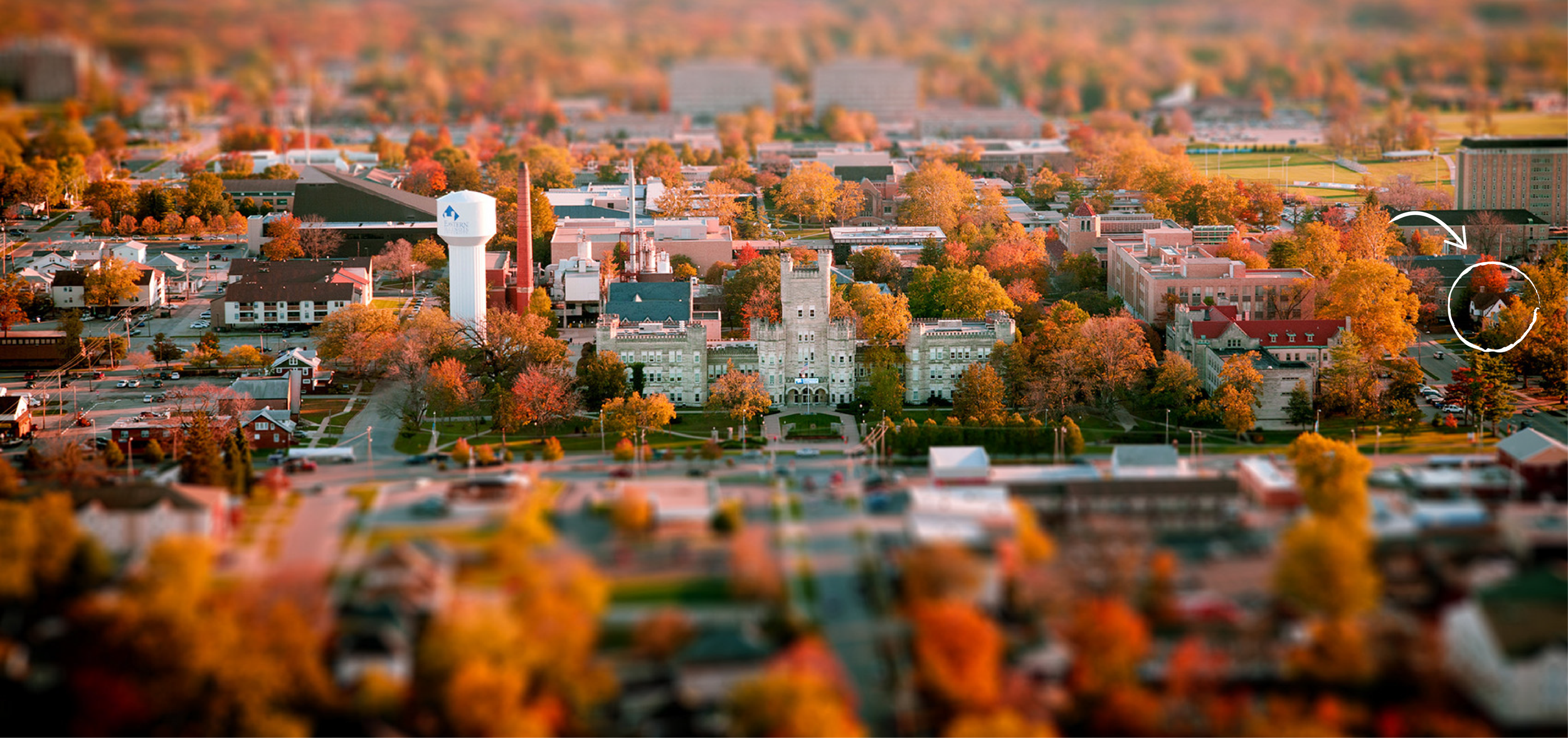 Aerial view of Eastern Illinois University in Charleston, Illinois, surrounded by vibrant autumn foliage, with a white arrow highlighting the HERC building.
