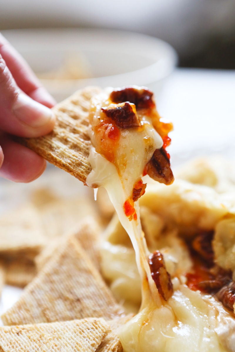 Triscuit cracker pulling cheesy bite of baked brie