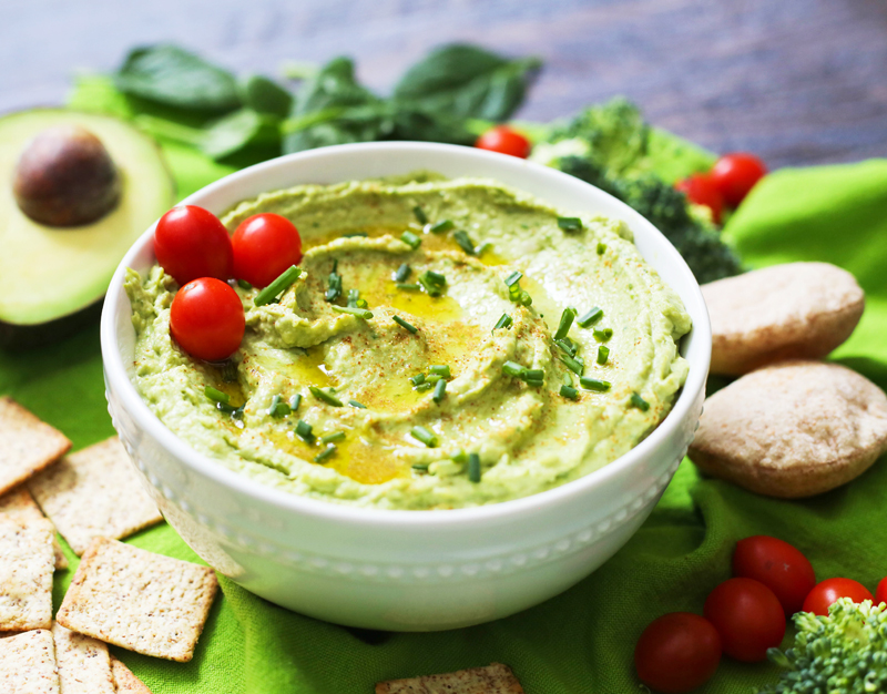 spinach hummus in a serving bowl surrounded by veggies