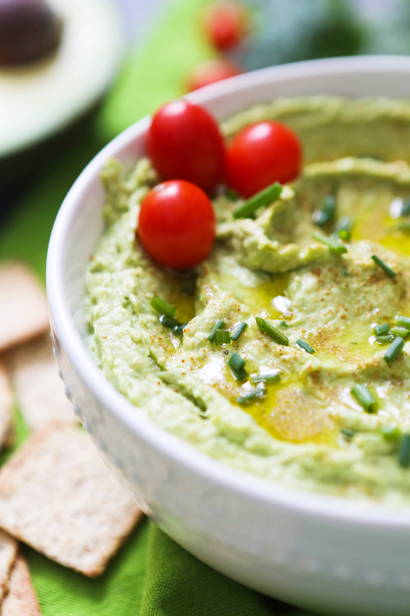 bowl of spinach hummus with cherry tomatoes sitting on top