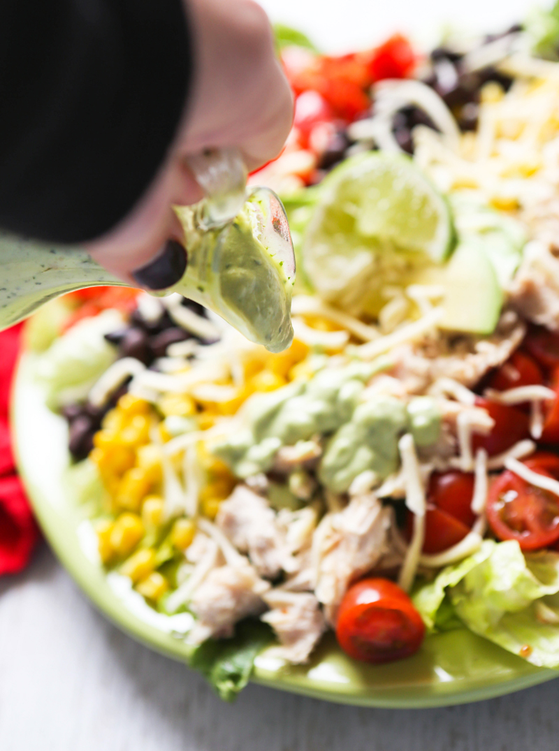 hand pouring avocado ranch dressing onto a plate of southwest chicken salad