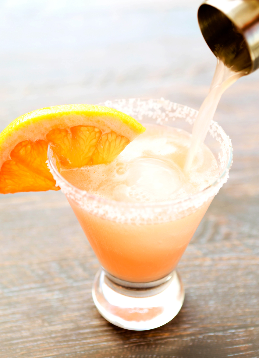 A salty dog drink being poured into a salted rimmed glass with a grapefruit rim