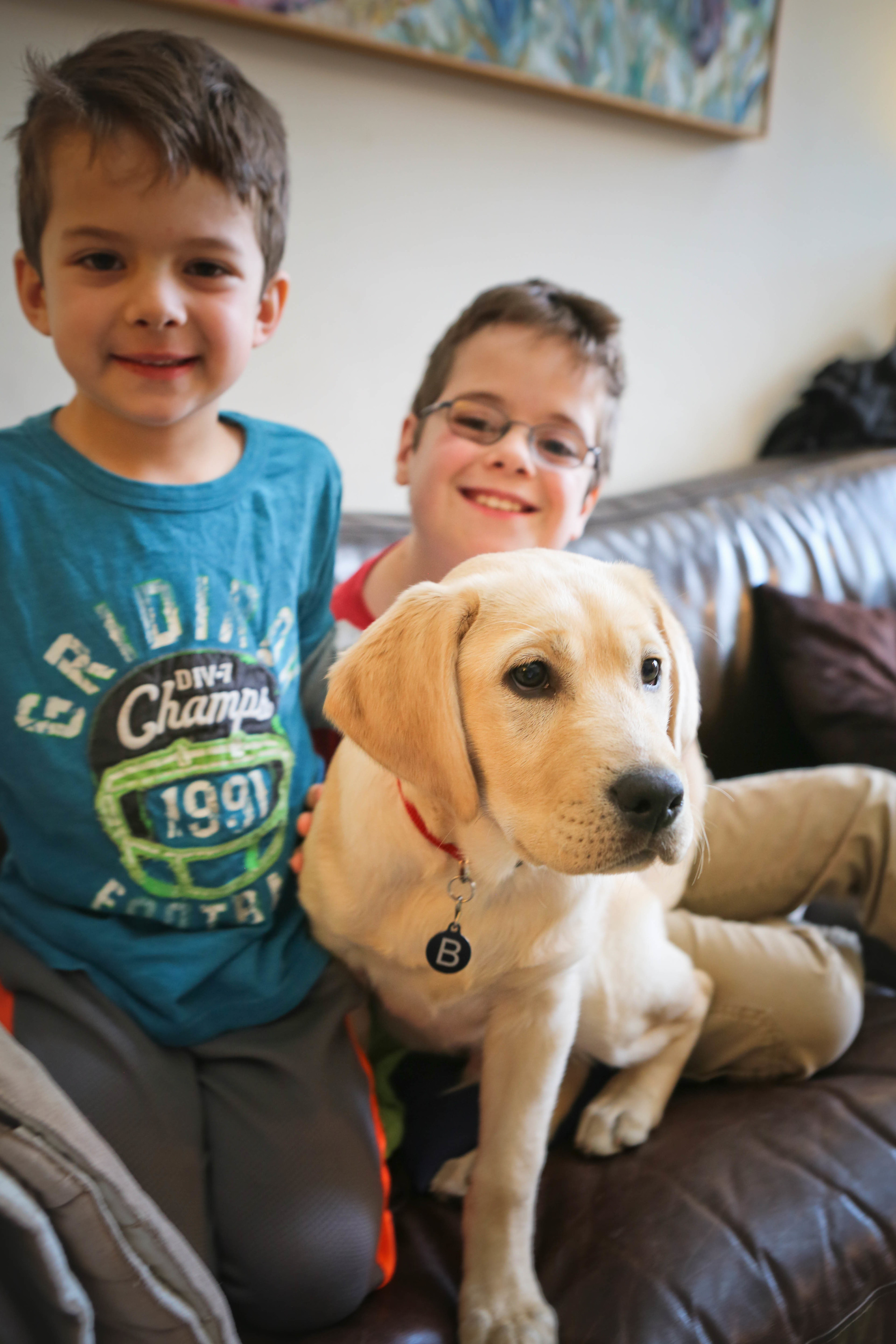 picture of 2 kids on a couch with their yellow lab puppy