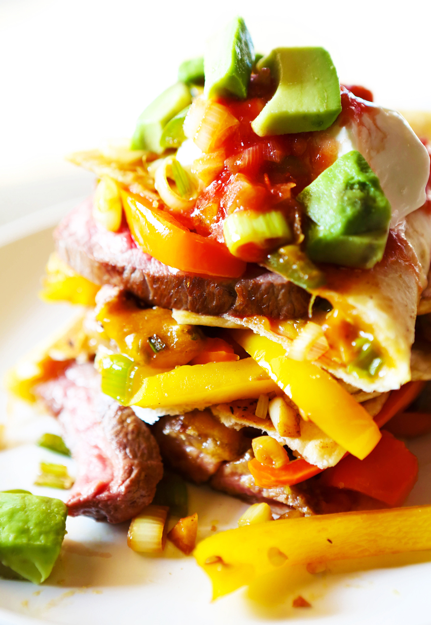 Close up of steak fajita quesadilla topped on one another  with veggies and avocado spilling out. 