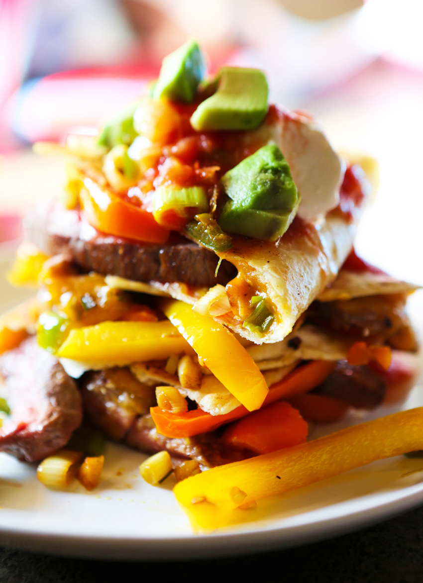 Close up of steak fajita quesadilla topped on one another  with veggies and avocado spilling out. 