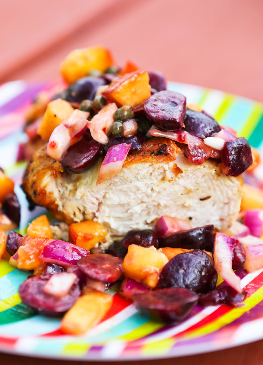 Close up of a grilled chicken piece cut in half and peach and cherry salsa spilling over it. 