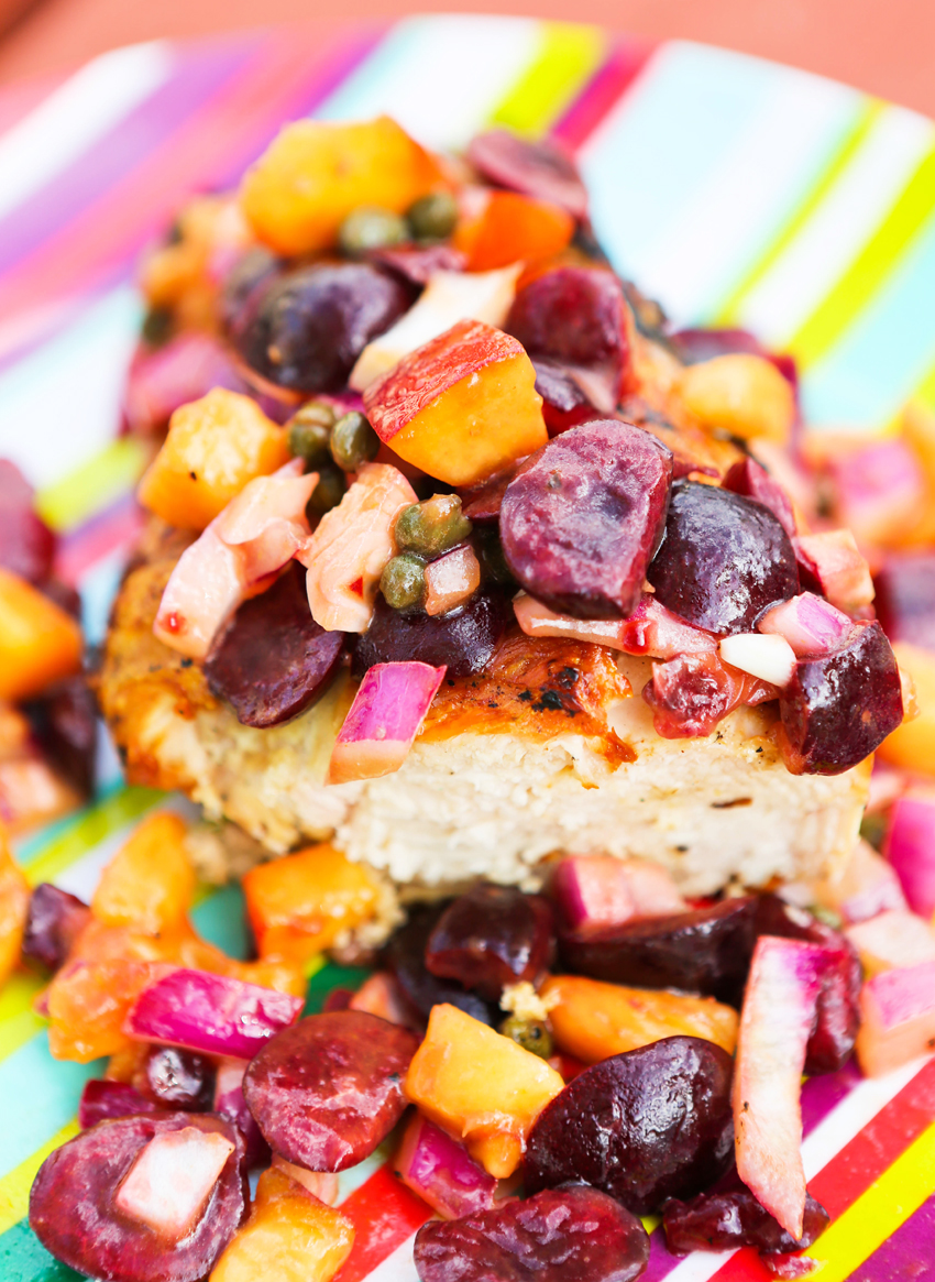 Close up of a grilled chicken piece cut in half and peach and cherry salsa spilling over it. 