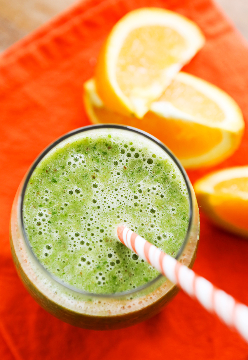 Top view of a glass of orange banana smoothie with a paper straw in it and sliced oranges on the table