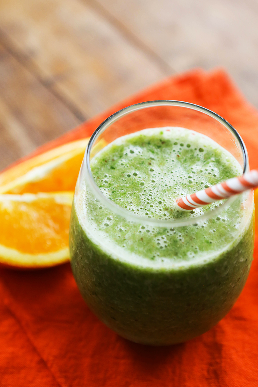 side view of a glass of orange banana smoothie with a paper straw and an orange slice next to it