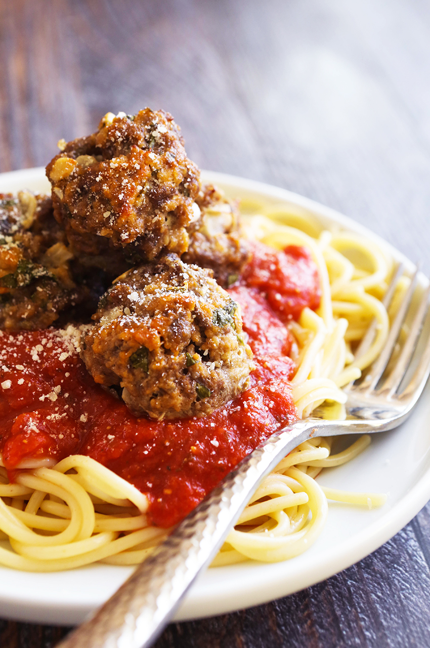 Plate of pasta, spaghetti sauce and three easy baked meatballs on top with a fork on the side of the plate