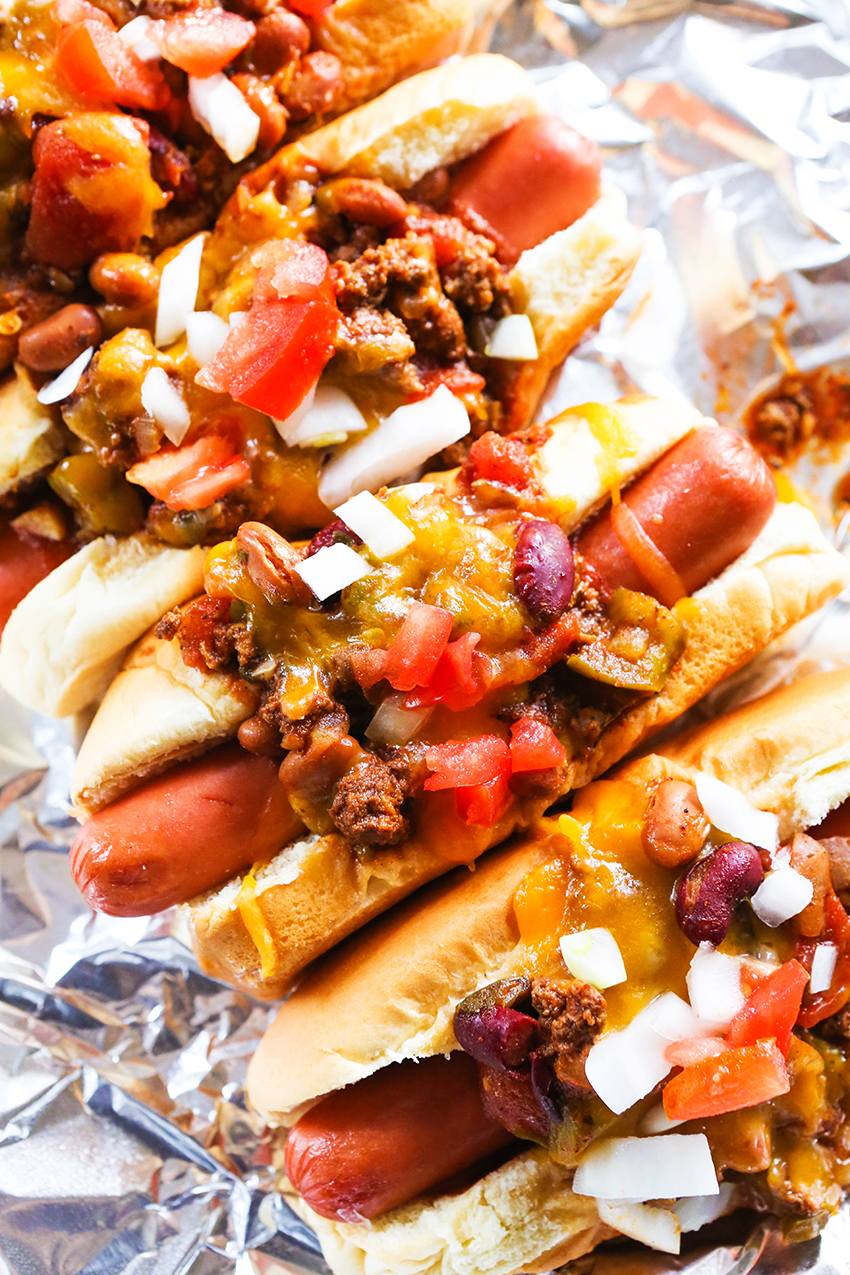 Hot dogs in buns lined up on foil with chili on the tops.