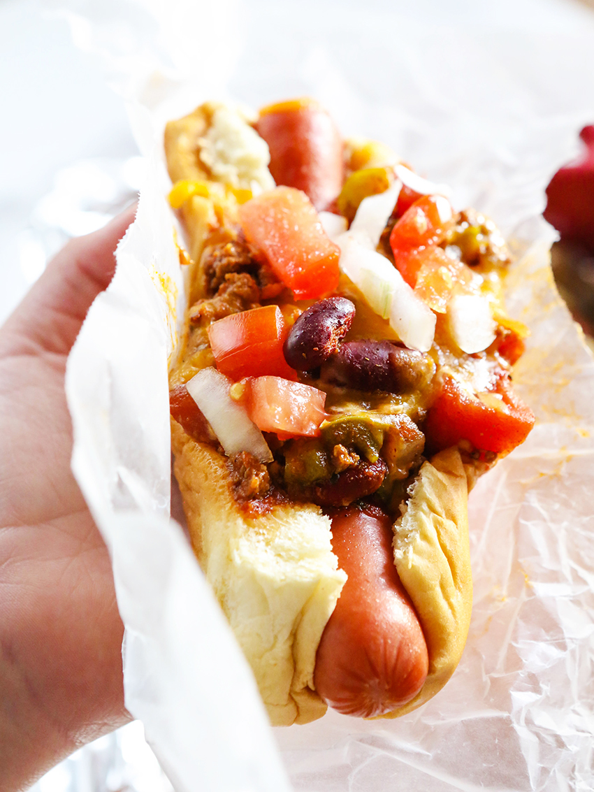 Hand holding a chili dog with all the fixins on top.