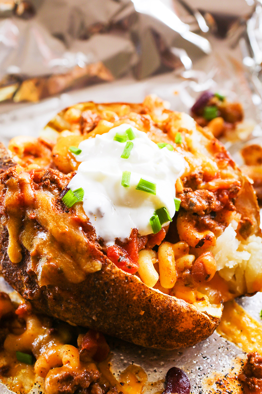 Close-up photo of a baked potato loaded with chili mac and sour cream.