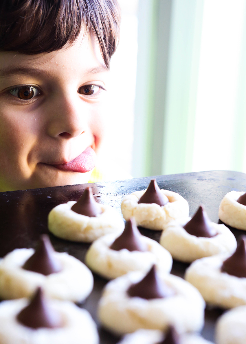 cute boy staring longingly at a tray of cream cheese cookies