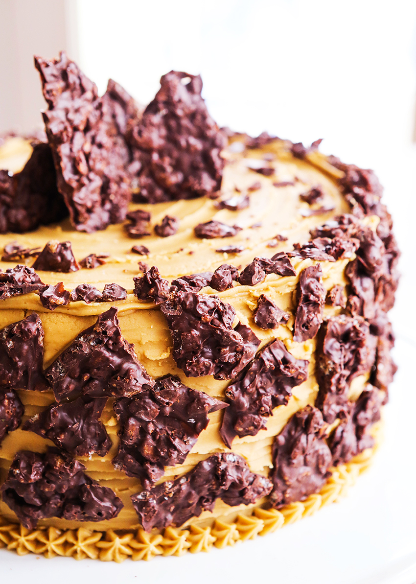 caramel frosting covered layer cake with crunch chocolate pieces on outside