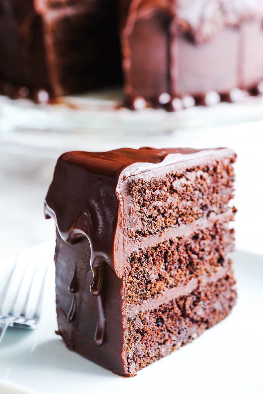 slice of triple layer chocolate cake on a white plate with ganache dripping over top and sides