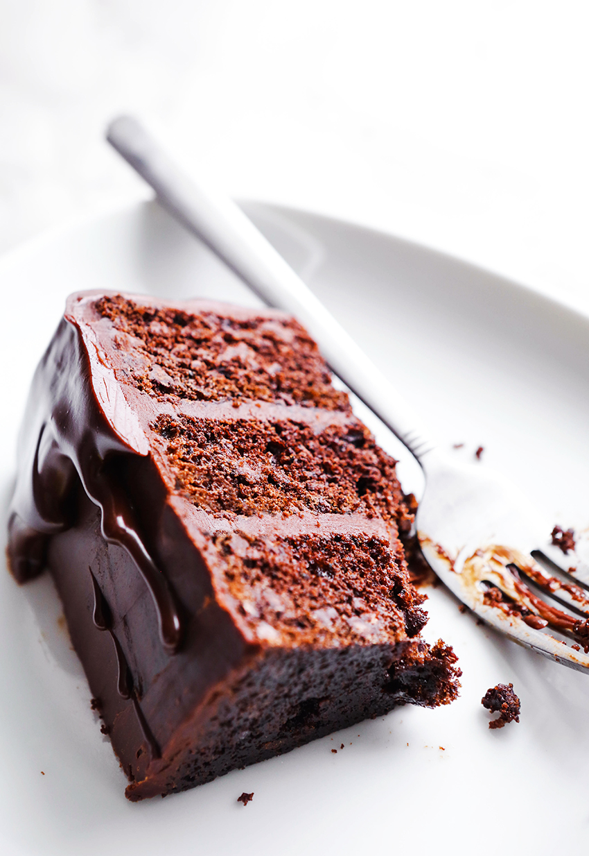 slice of triple layer chocolate cake on a white plate with bite taken out