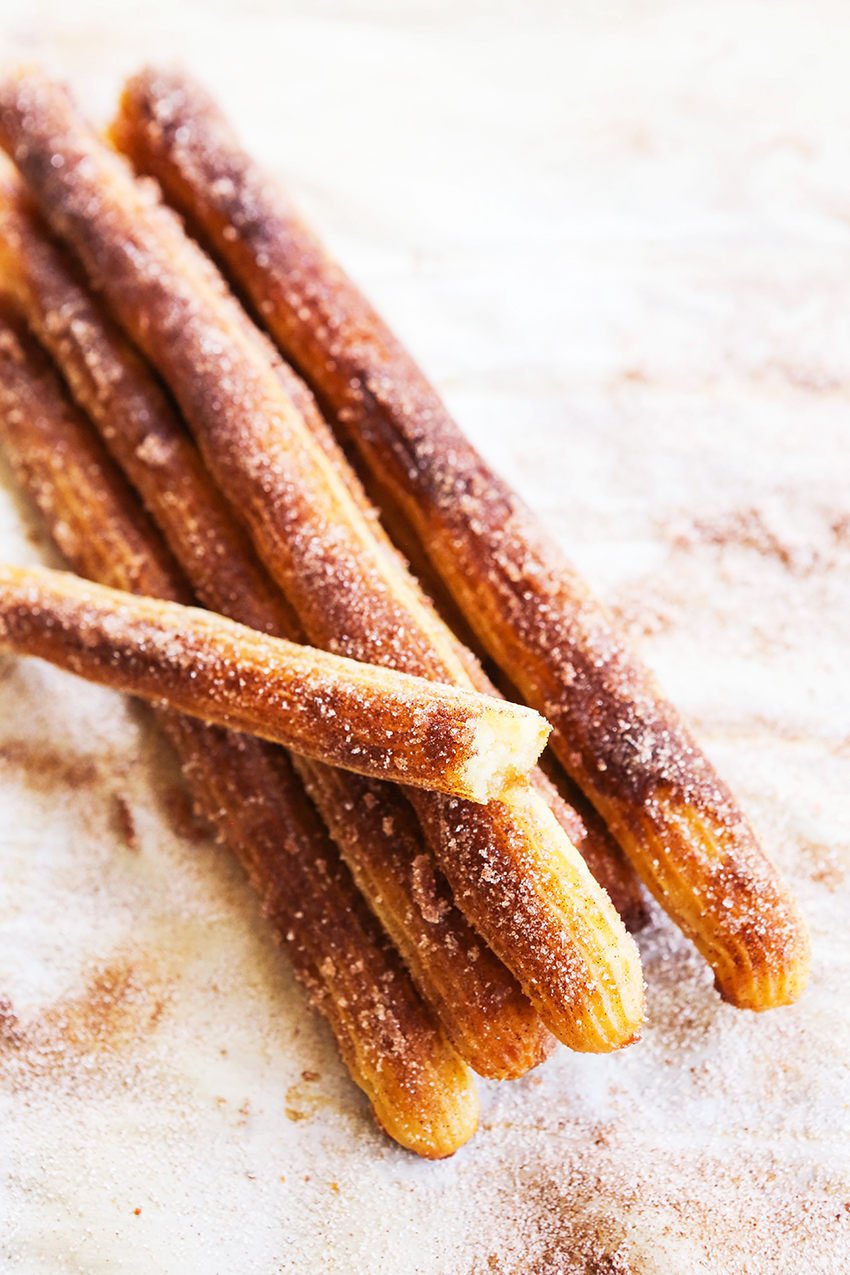 sugary churros stacked in a pile on parchment