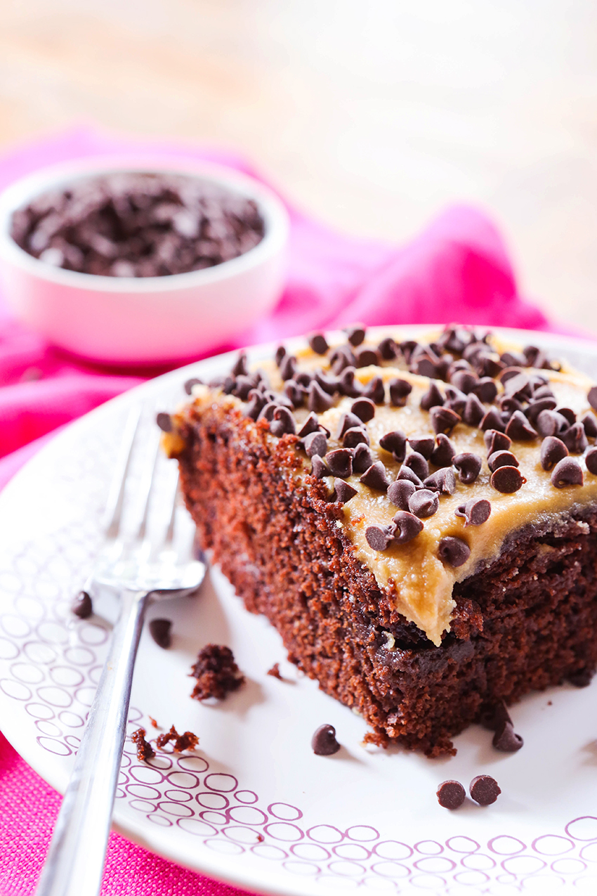 slice of chocolate cake with caramel frosting sitting on a plate with a fork nearby