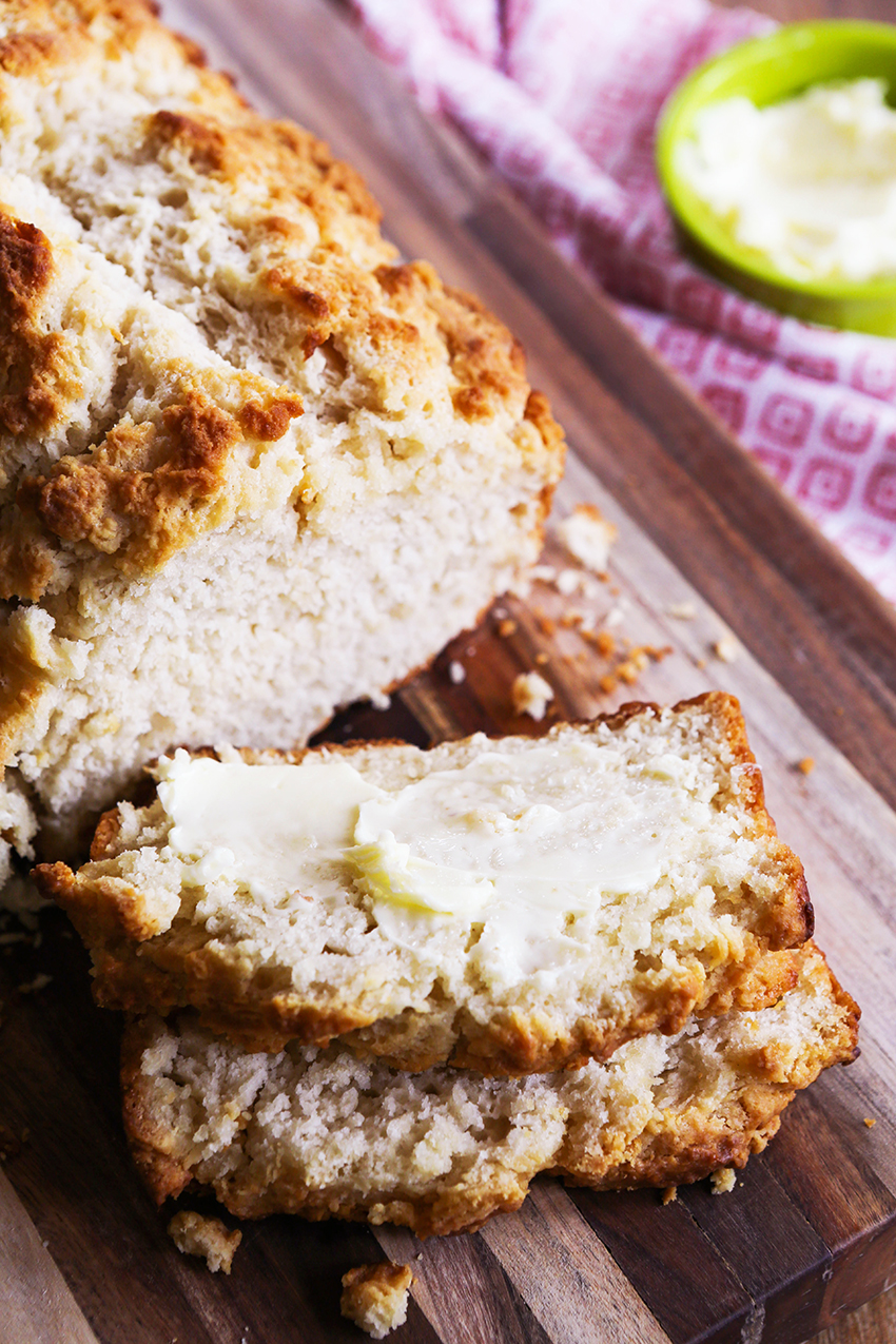 loaf of beer bread cut into slices and a top slice buttered, ready to eat