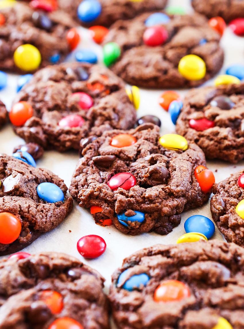 chocolate M&M cookies lined up on a baking sheet with M&M's scattered