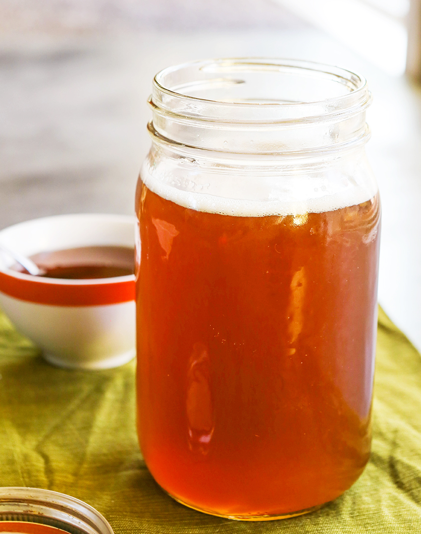 Open glass jar of simple syrup with  honey with a bowl of honey in background