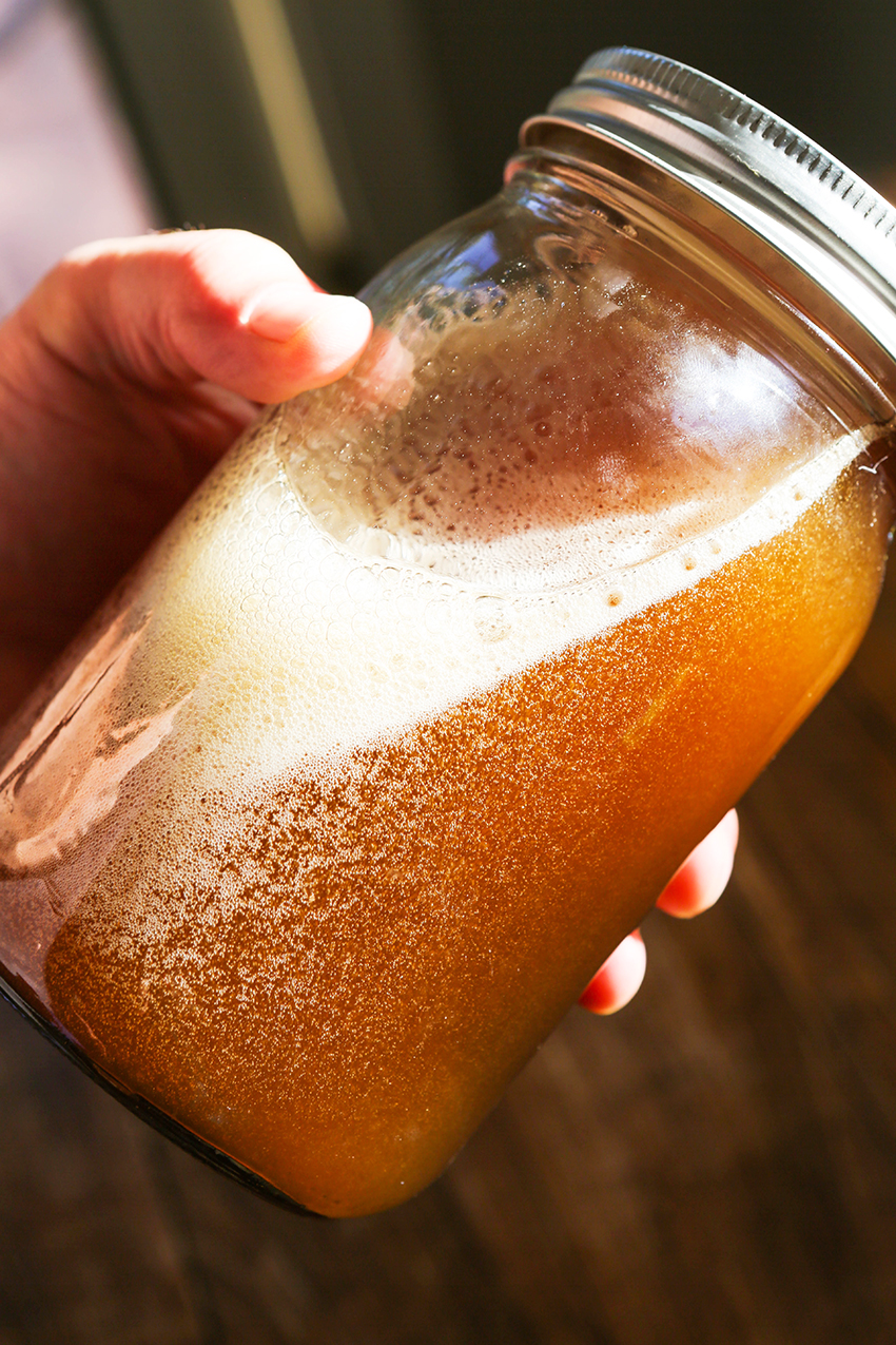 Hand holding a tilted glass bottle of simple syrup with honey