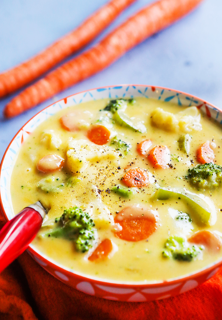 Comforting bowl of cheesy vegetable soup alongside a couple carrots