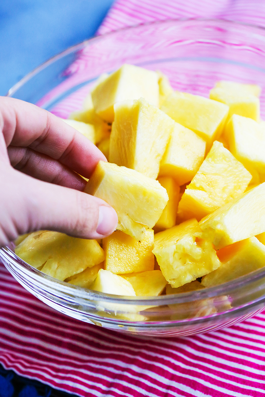 hand reaching into a bowl of pineapple chunks