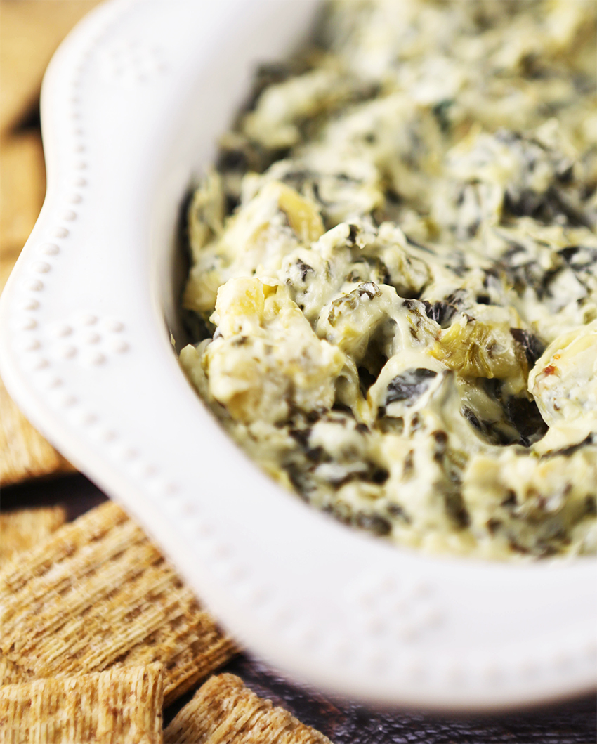 close up of gooey crockpot spinach artichoke dip surrounded by crackers