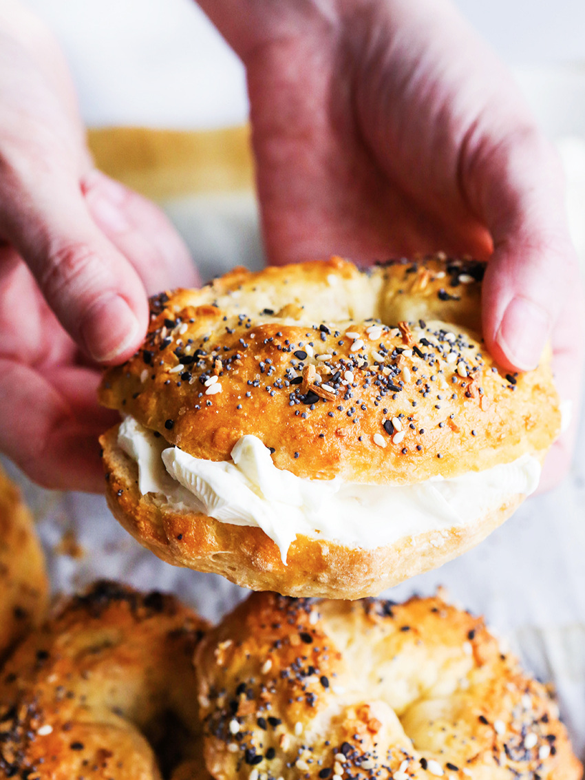 hands holding out a bagel with cream cheese oozing out the center