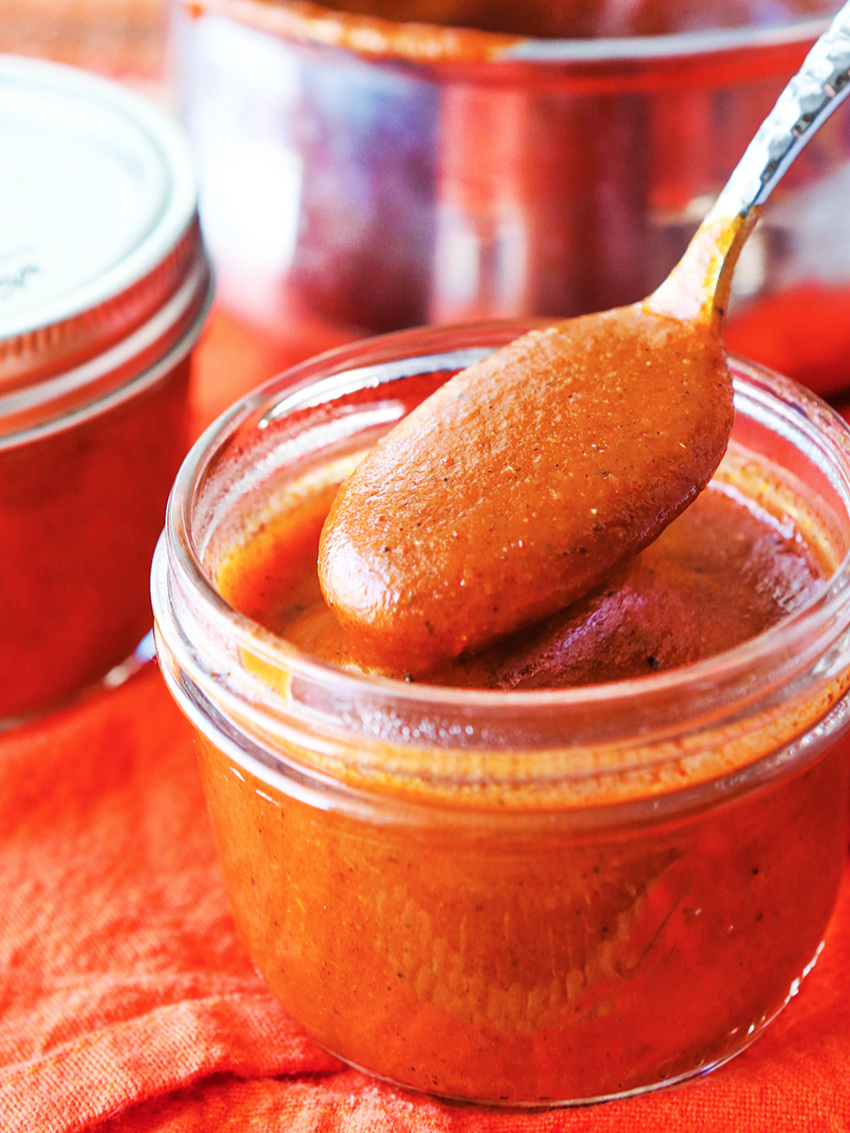  A spoonful of homemade enchilada sauce being held over jar 