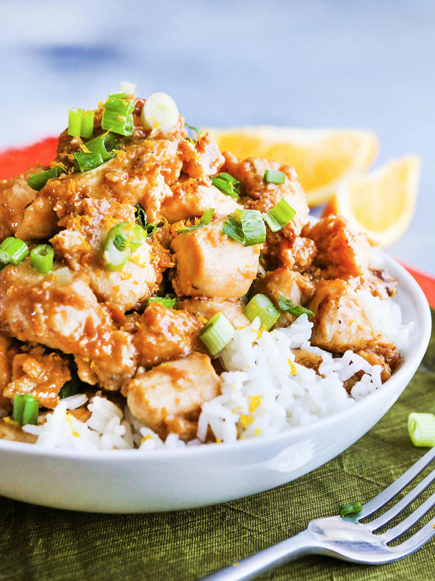 Close up of bowl with white rice and orange chicken with a fork on the side