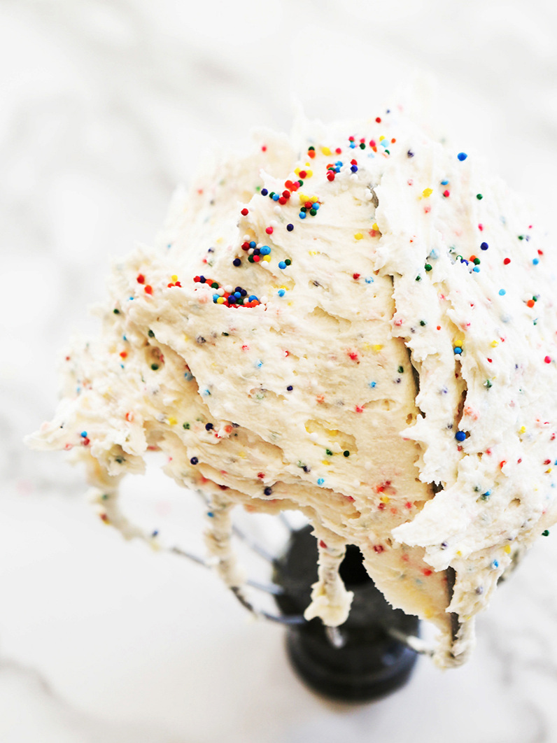 Wire whisk standing upright filled with confetti colored vanilla buttercream frosting