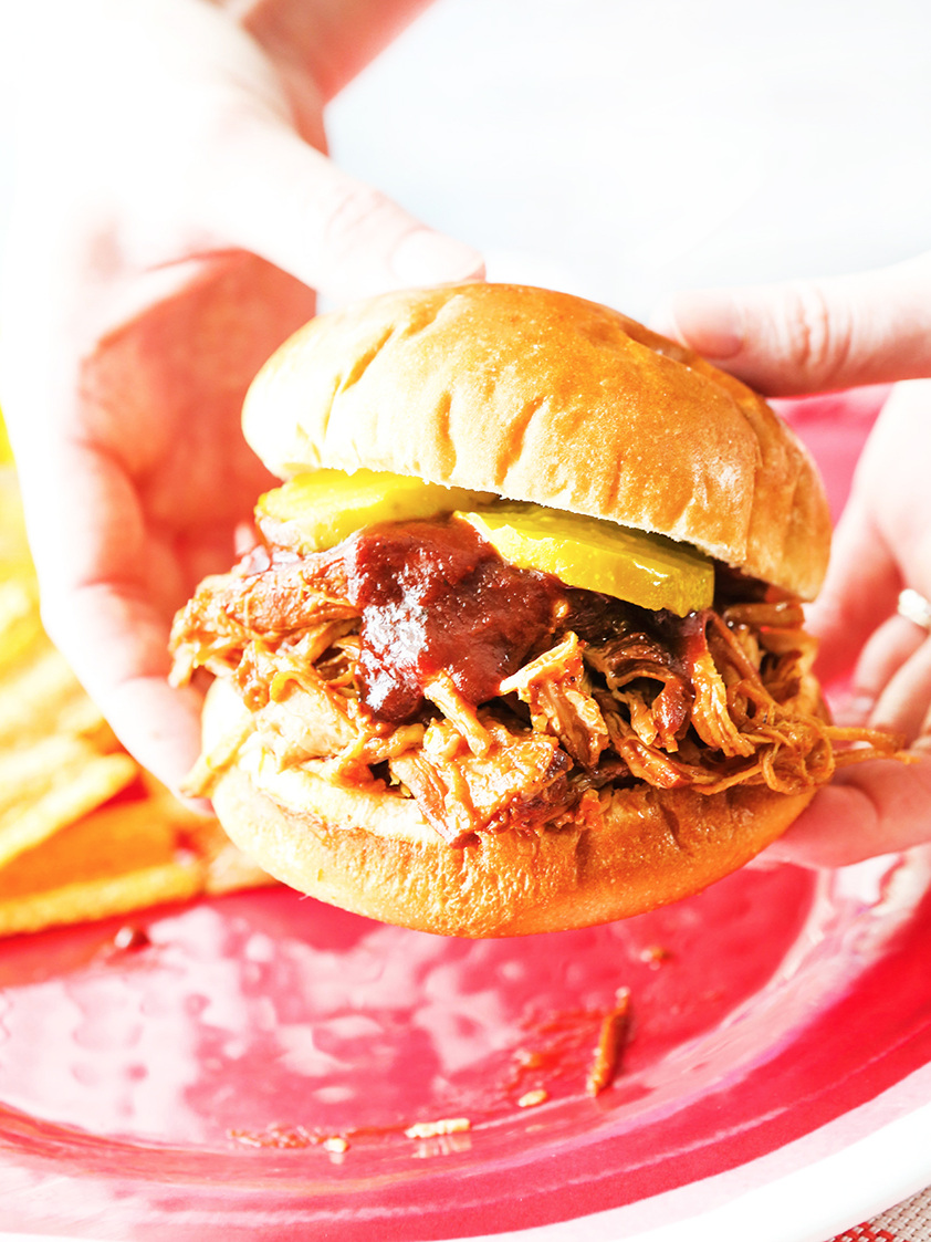  Hands holding bbq pulled pork sandwich with bbq sauce dripping out the sides 