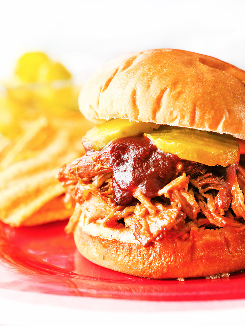  Pulled pork sandwich on a plate with bbq sauce dripping out of buns 
