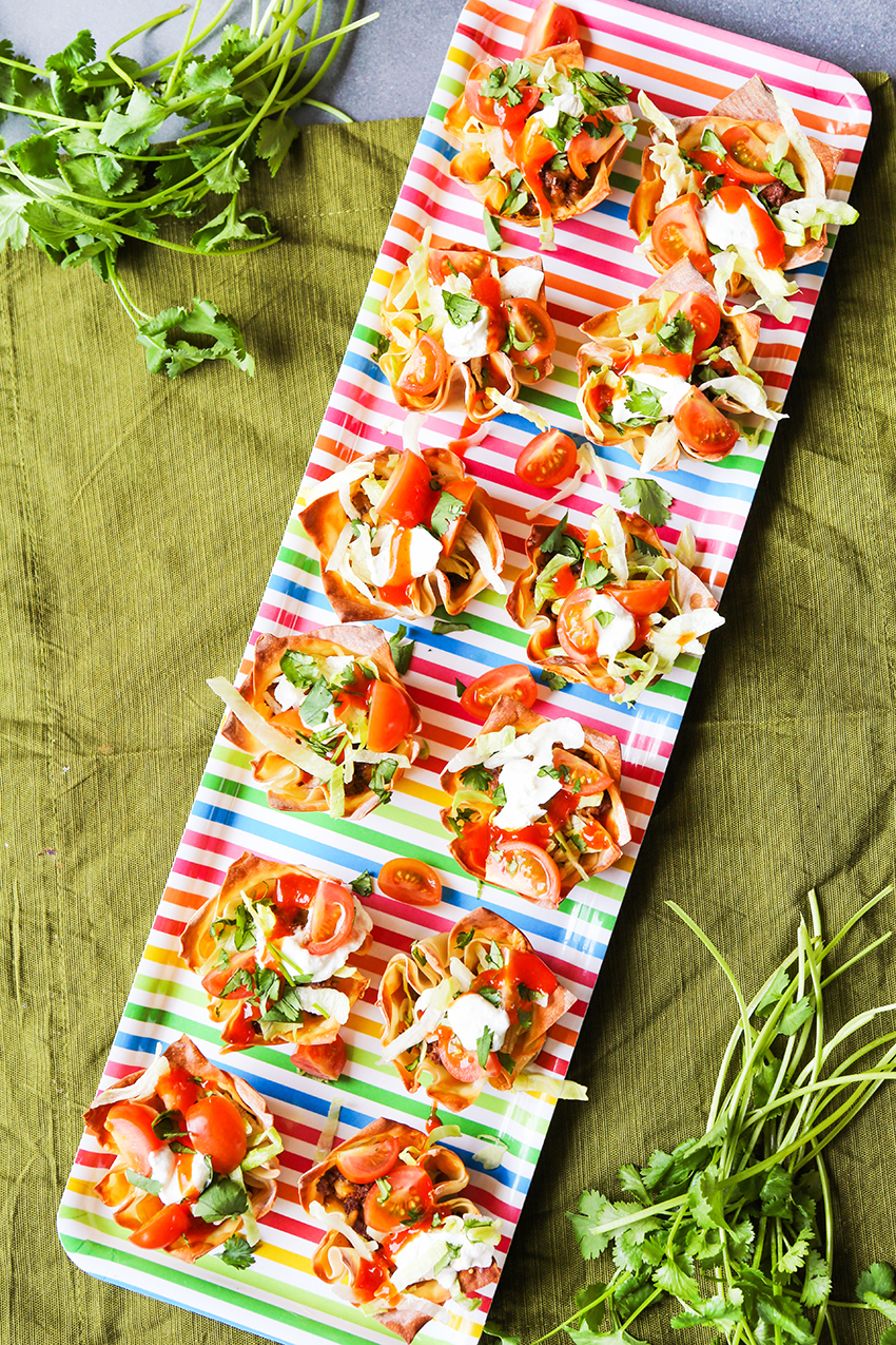 Colorful tray of prepared taco cups sitting on a table cloth with a sprig of cilantro next to it. 